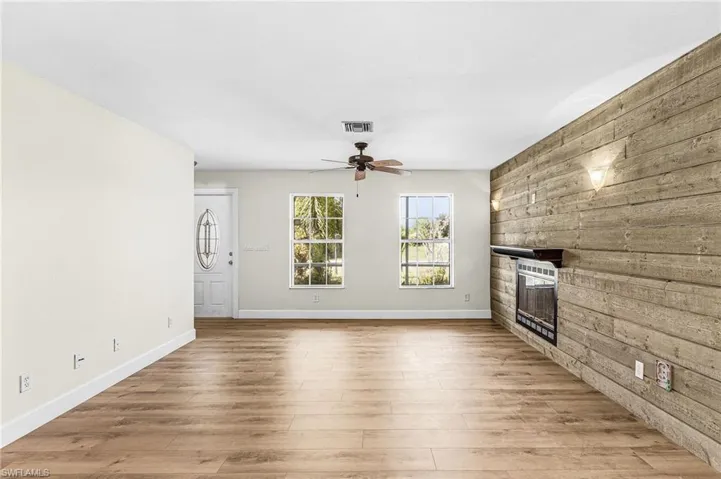 Wood-finish flooring, two windows, ceiling fan, decorative wall paneling, and an electric fireplace