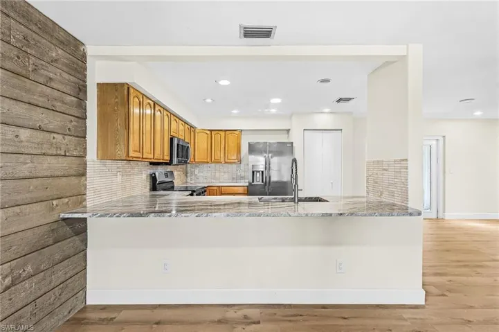 Kitchen featuring granite countertops, wood cabinetry, stainless steel appliances, and a tiled backsplash