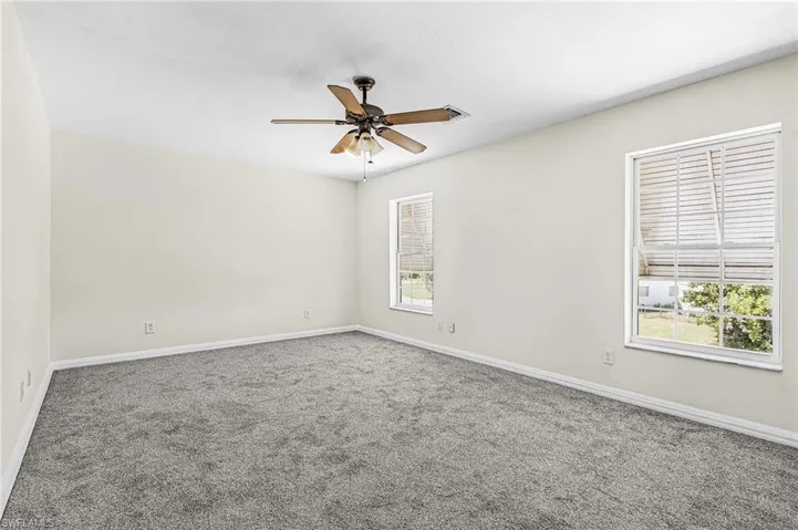 Spacious room featuring gray carpeting, white walls, two windows with blinds, and a ceiling fan