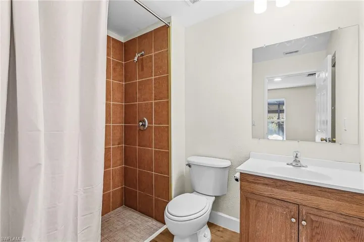 Bathroom featuring a shower with tile surround, a toilet, a vanity with a white countertop and integrated sink, and wood-finish flooring