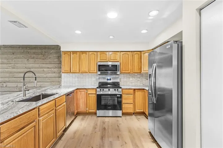 Kitchen featuring wood cabinetry, stainless steel appliances, a tile backsplash, and light wood-finish flooring