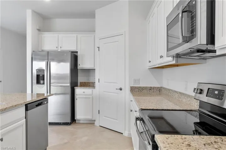 Kitchen with stainless steel appliances, white cabinetry, and light stone counters