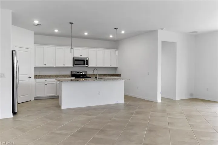 Kitchen with white cabinets, stainless steel appliances, light stone counters, hanging light fixtures, and an island with sink