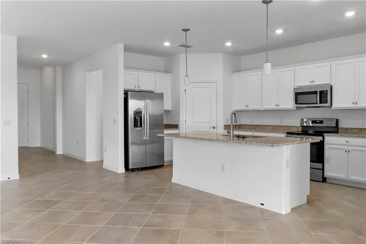 Kitchen with stainless steel appliances, light stone counters, white cabinets, a kitchen island with sink, and hanging light fixtures