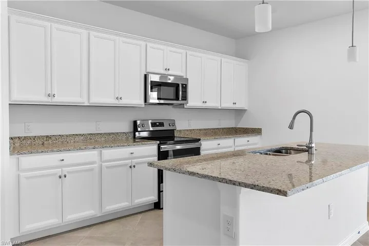 Kitchen featuring stainless steel appliances, light stone countertops, white cabinetry, and pendant lighting