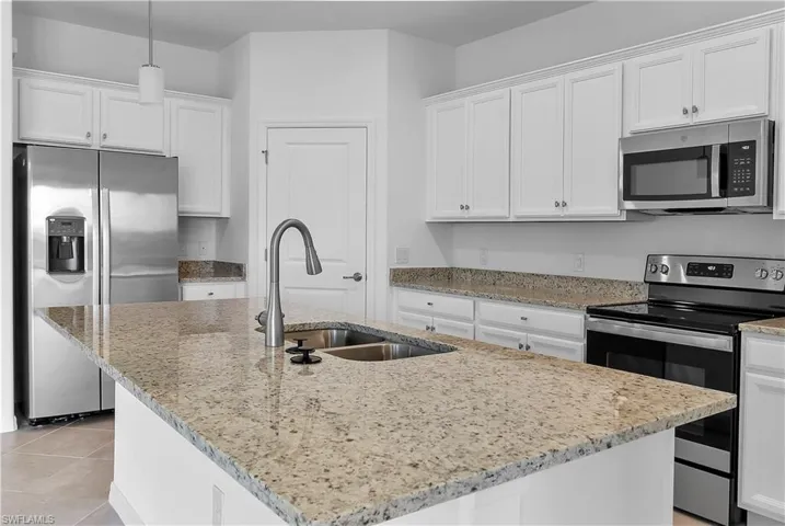 Kitchen featuring stainless steel appliances, white cabinetry, and a center island with sink