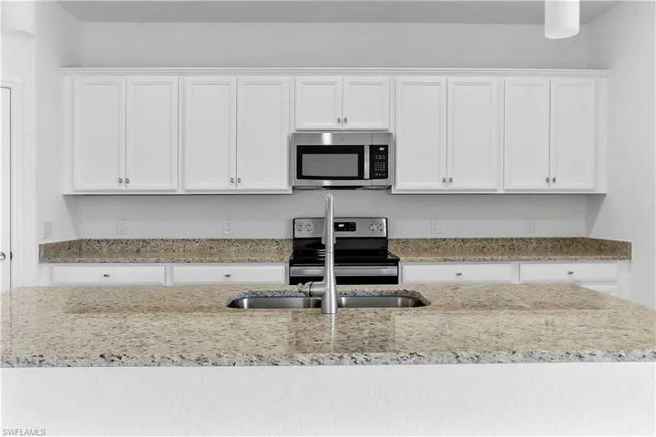 Kitchen with white cabinets, stainless steel appliances, and light stone counters
