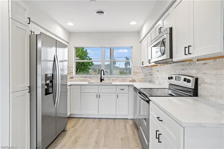 Kitchen with appliances with stainless steel finishes, white cabinetry, light wood finished floors, tasteful backsplash, and recessed lighting