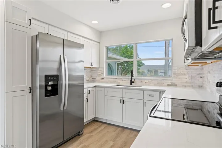 Kitchen with stainless steel appliances, white cabinetry, light stone counters, light wood-type flooring, and recessed lighting