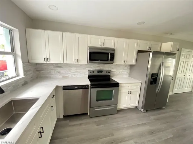 Kitchen with stainless steel appliances, white cabinets, light wood-style floors, light stone countertops, and decorative backsplash