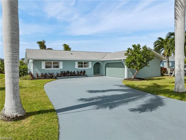 Ranch-style home with an attached garage, driveway, a front yard, and stucco siding