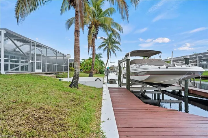 Dock area with boat lift, a sunroom, a yard, glass enclosure, and a water view
