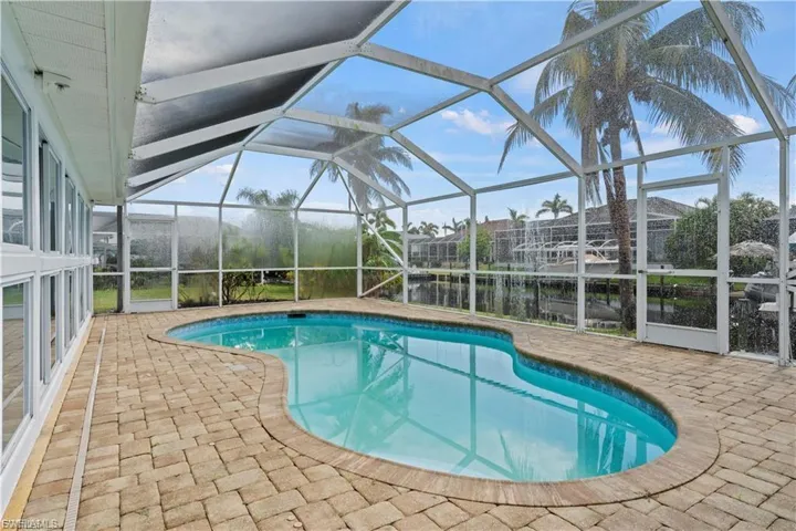 Outdoor pool featuring glass enclosure, a patio, a sunroom, and a water view