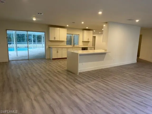 Kitchen featuring open floor plan, white cabinetry, wood finished floors, light countertops, and recessed lighting
