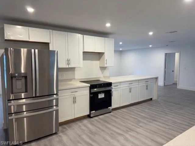 Kitchen with stainless steel fridge with ice dispenser, black electric range oven, light wood-style flooring, white cabinets, and light countertops