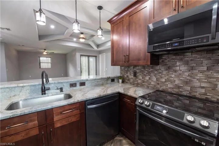 Kitchen with black appliances, ceiling fan, hanging light fixtures, sink, and kitchen peninsula
