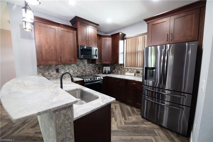 Kitchen featuring appliances with stainless steel finishes, pendant lighting, backsplash, light stone countertops, and dark parquet flooring