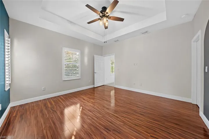 Unfurnished bedroom featuring a tray ceiling, dark wood finished floors, and a ceiling fan