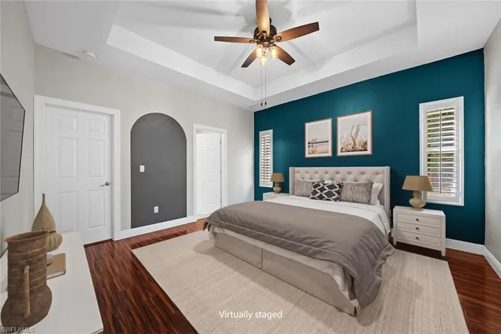 Bedroom featuring a raised tray ceiling, dark wood-type flooring, and ceiling fan