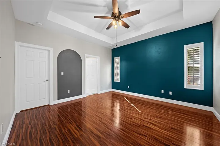 Unfurnished room featuring a tray ceiling, dark wood-type flooring, and a ceiling fan