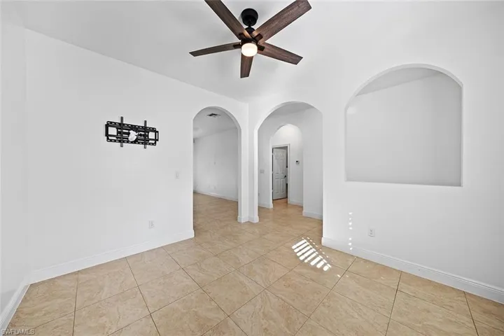 Empty room featuring arched walkways, a ceiling fan, and light tile patterned flooring