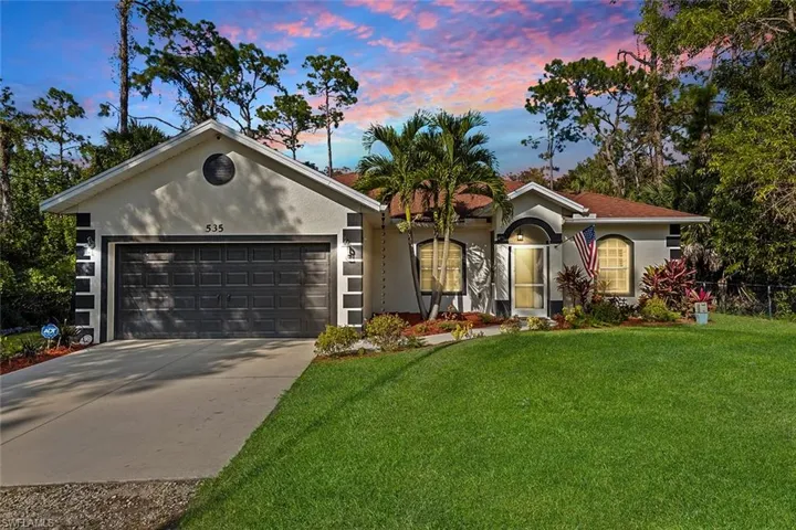 View of front of property featuring stucco siding, a lawn, driveway, and an attached garage