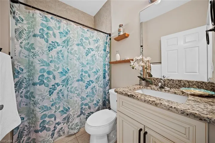 Bathroom with vanity, granite counter and light tiled wall to the ceiling and on the floor in a light pattern