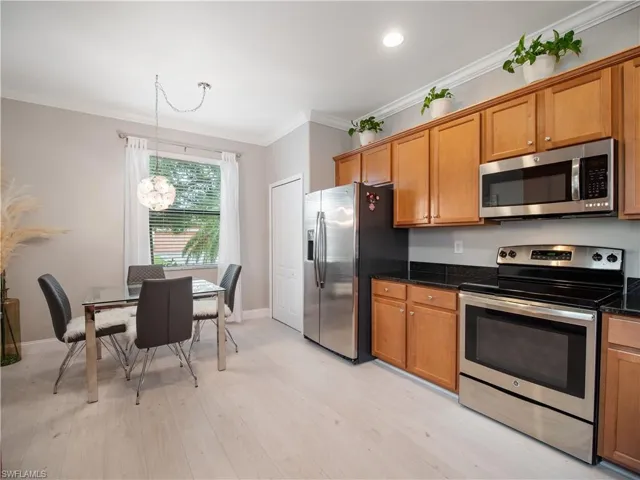 Kitchen featuring light hardwood / wood-style flooring, dark stone counters, appliances with stainless steel finishes, pendant lighting, and ornamental molding