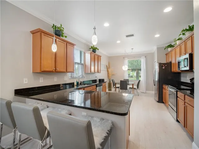 Kitchen with appliances with stainless steel finishes, light hardwood / wood-style flooring, kitchen peninsula, hanging light fixtures, and a kitchen breakfast bar