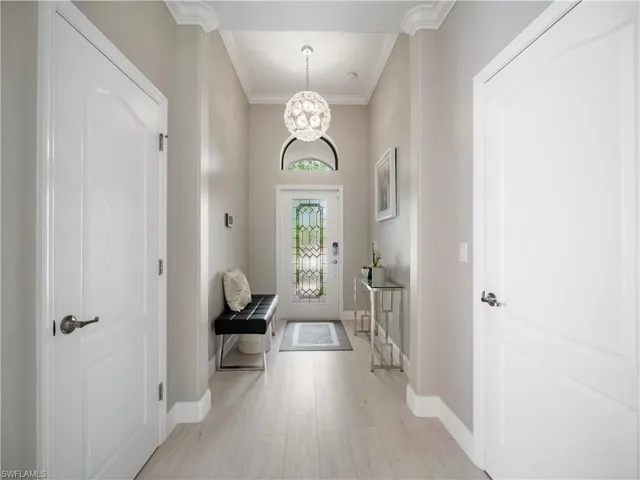 Foyer with ornamental molding, light wood-type flooring, and a chandelier