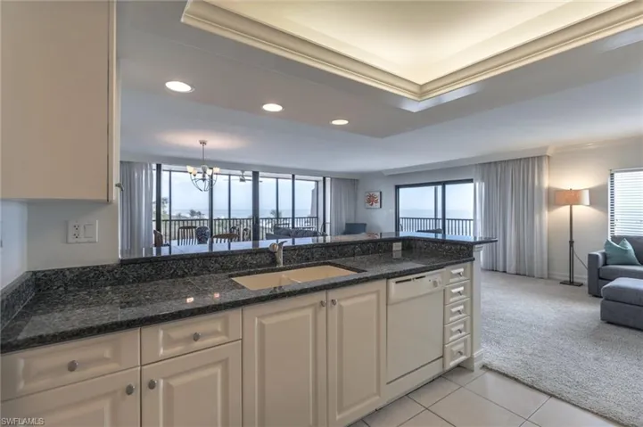 Kitchen featuring white cabinets, light colored carpet, sink, dark stone countertops, and dishwasher