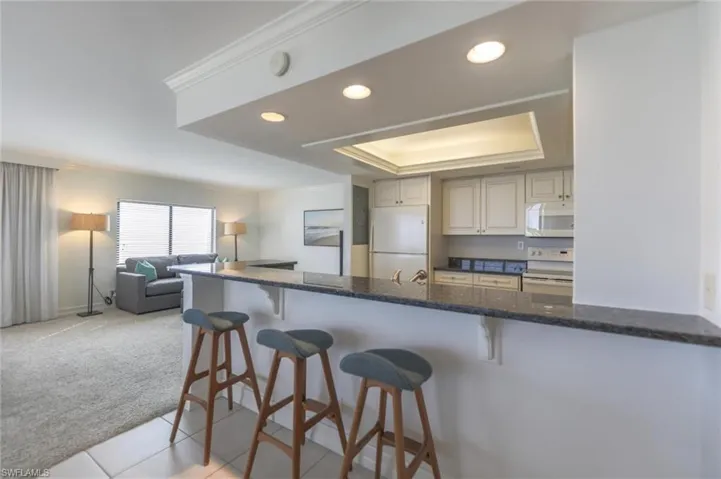 Kitchen featuring a breakfast bar area, kitchen peninsula, white appliances, a tray ceiling, and light carpet