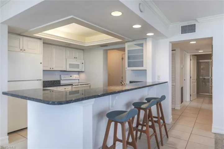 Kitchen featuring white cabinetry, kitchen peninsula, white appliances, light tile patterned floors, and ornamental molding