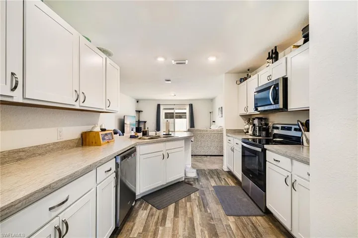 Kitchen with white cabinets, appliances with stainless steel finishes, open floor plan, dark wood-type flooring, and a peninsula
