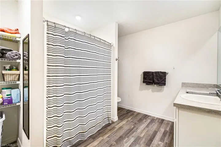 Bathroom with a shower with shower curtain, baseboards, toilet, wood finished floors, and vanity