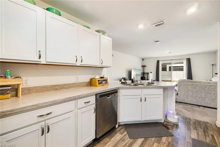 Kitchen featuring stainless steel dishwasher, light countertops, open floor plan, dark wood finished floors, and a peninsula