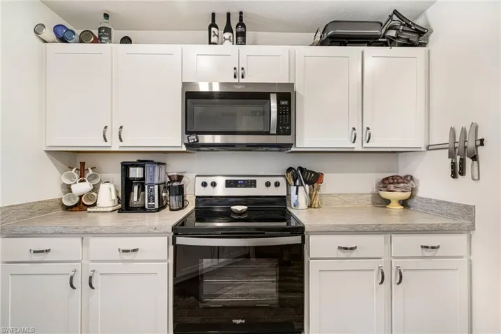 Kitchen featuring stainless steel microwave, white cabinetry, electric range, and light countertops