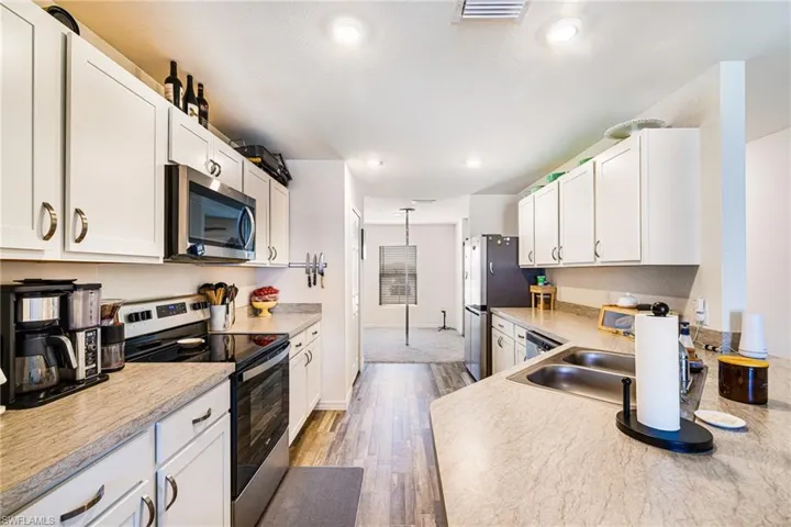 Kitchen with stainless steel appliances, light wood-type flooring, visible vents, white cabinetry, and light countertops