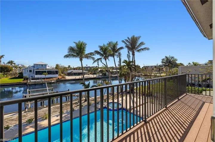 Balcony with wood-finish decking and metal railing, overlooking a sparkling blue pool and a canal with a dock