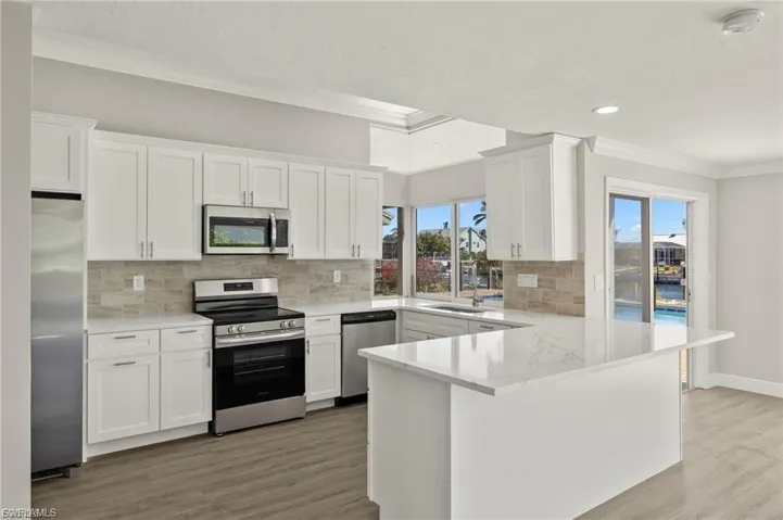 Open-concept kitchen featuring white shaker cabinetry, stainless steel appliances, a light-toned tile backsplash, and a large central island with a solid surface countertop