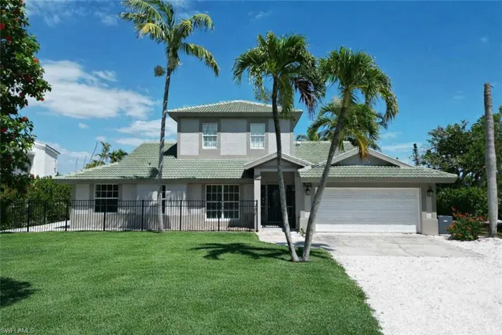 Two-story stucco residence featuring a green tile roof, an integrated two-car garage, and a large front lawn