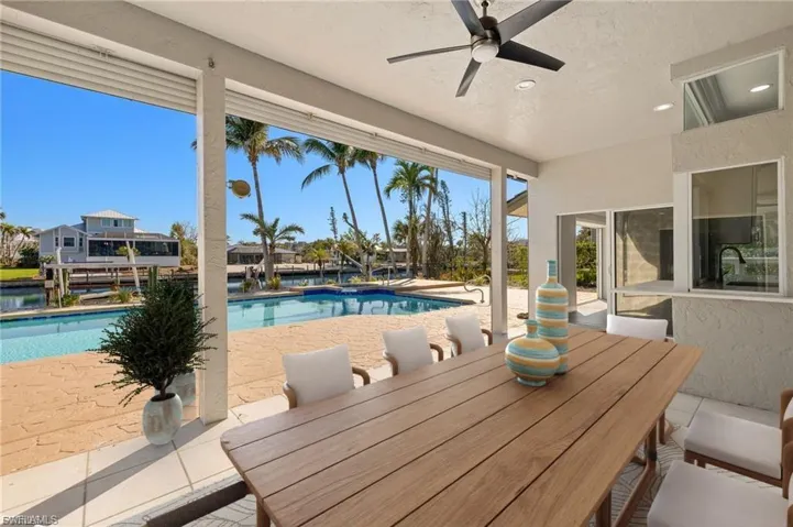 Covered outdoor living area featuring a wood-finish dining table and a ceiling fan