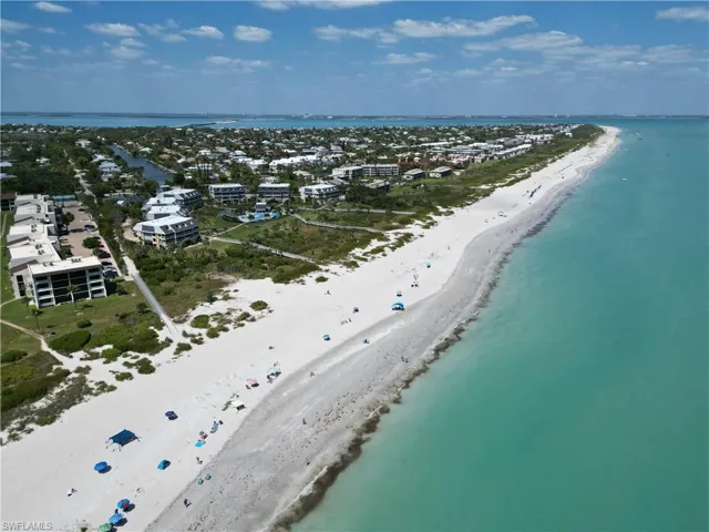 Expansive coastal setting featuring a wide sandy beach, turquoise waters, and a residential area with multiple buildings