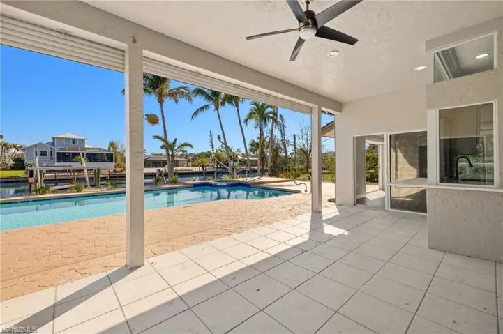 Outdoor covered patio featuring white tile flooring, a built-in outdoor kitchen area with a sink and countertop, and a ceiling fan