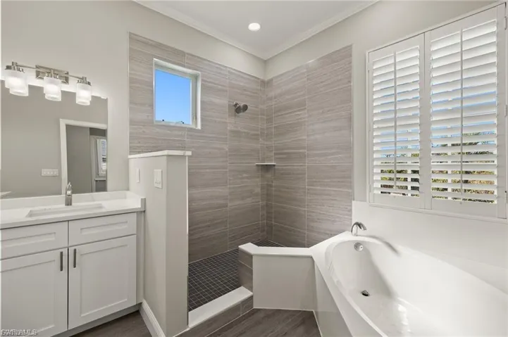 Modern bathroom featuring a freestanding tub, walk-in shower with tile surround, white vanity with quartz countertop, and plantation shutters
