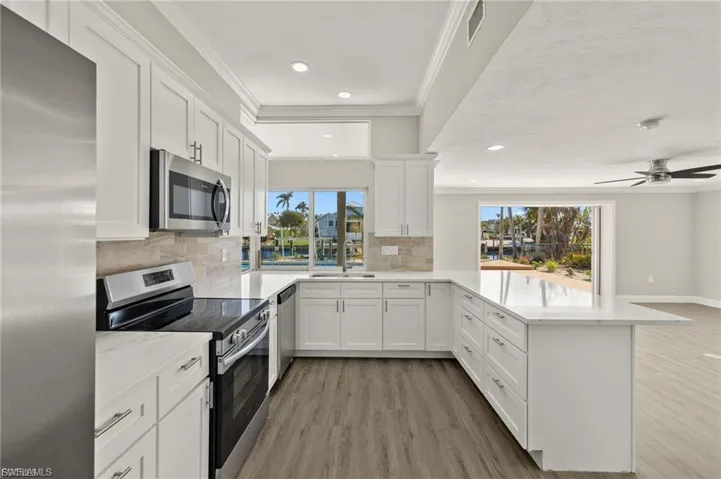 Bright kitchen featuring white cabinetry, stainless steel appliances, a tile backsplash, and a spacious island with a white countertop