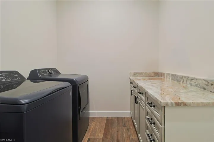 Laundry area featuring dark wood-style flooring, independent washer and dryer, and cabinet space