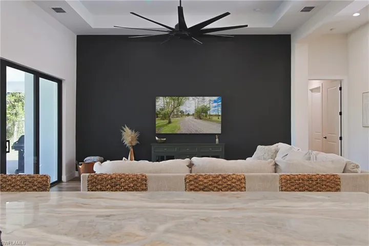 Living area with ceiling fan, an accent wall, wood finished floors, recessed lighting, and a high tray ceiling