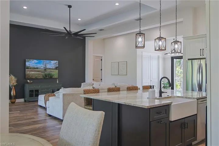 Two tone kitchen with a breakfast bar, open floor plan, light stone counters, decorative light fixtures, and stainless steel appliances