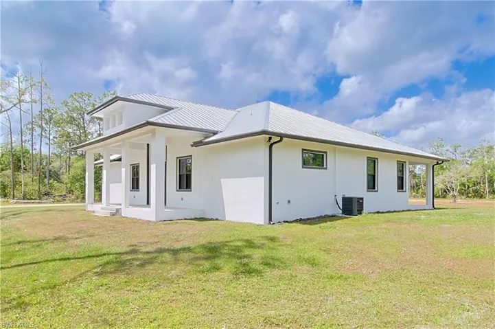 Back of property featuring a lawn, a metal roof, and stucco siding